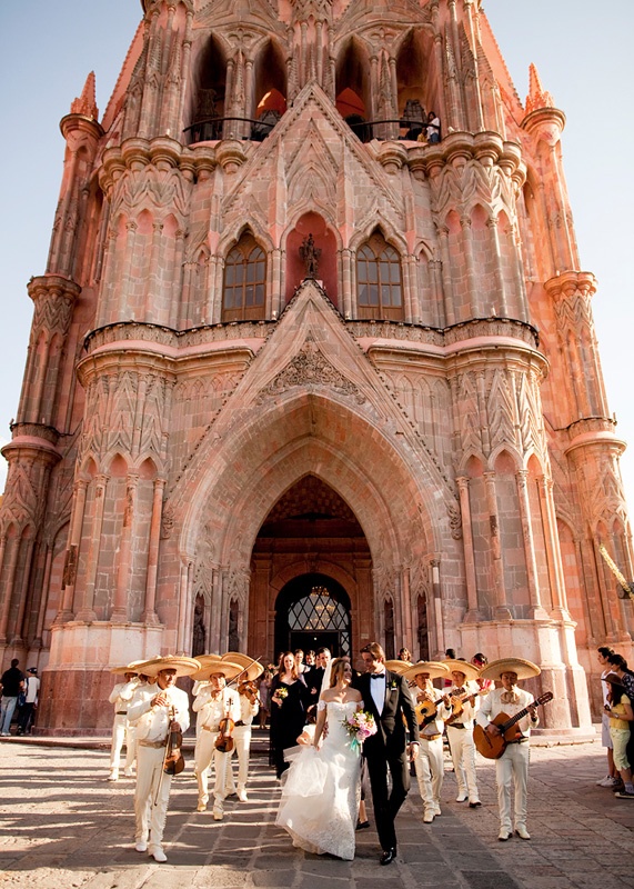 Mariachis leading a couple out of a pink stone church