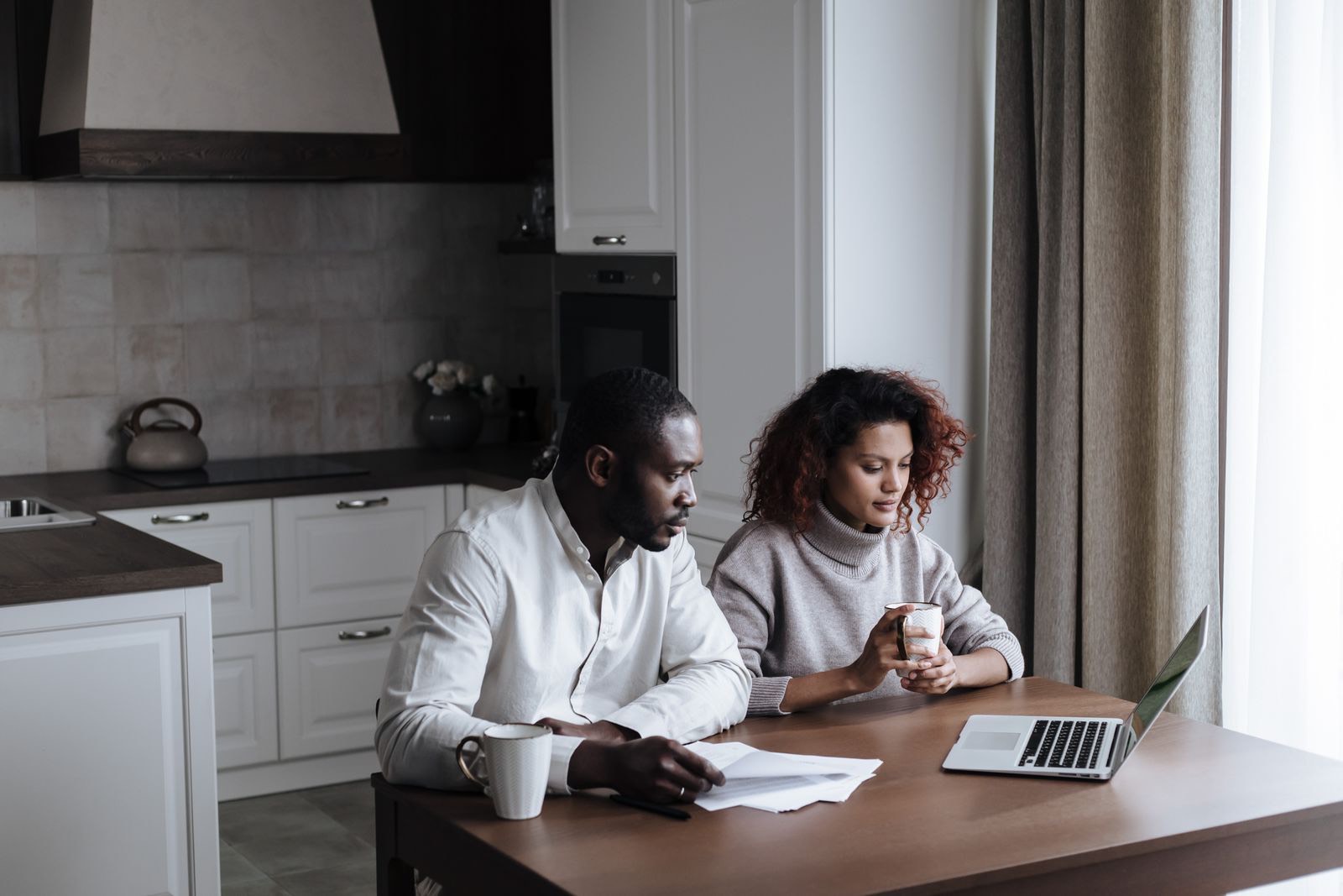 A couple planning their wedding together on a laptop at home in warm afternoon light