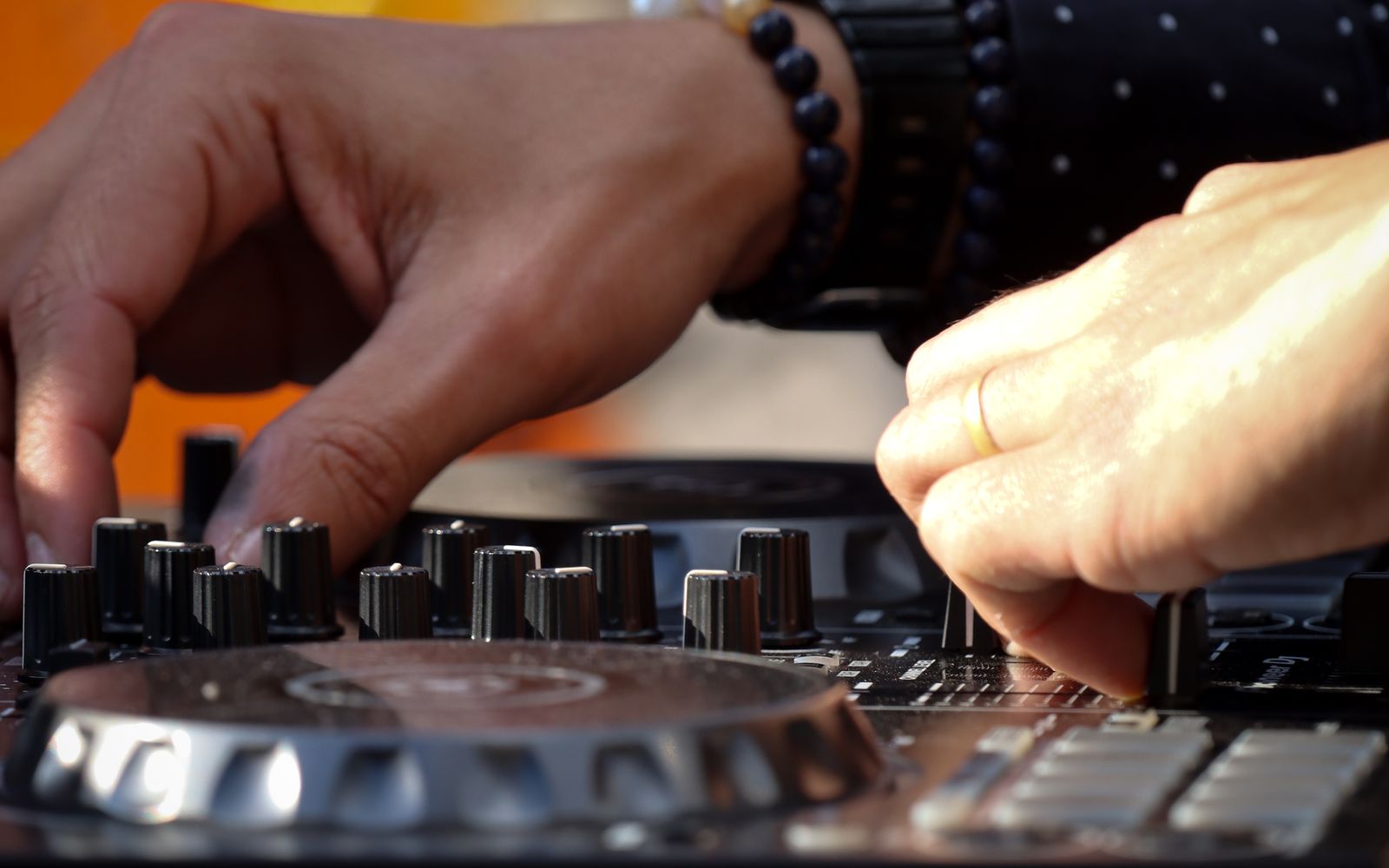 A wedding DJ mixing on a controller in warm light, a wedding ring visible on one hand