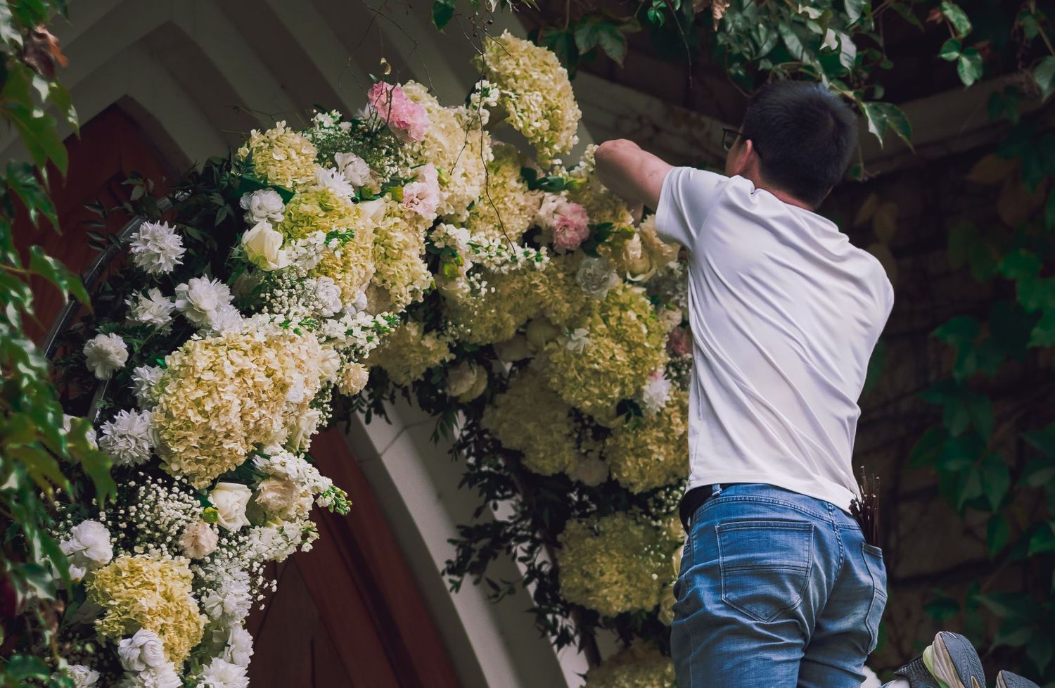 A florist building a lush hydrangea and rose flower arch by hand at a wedding