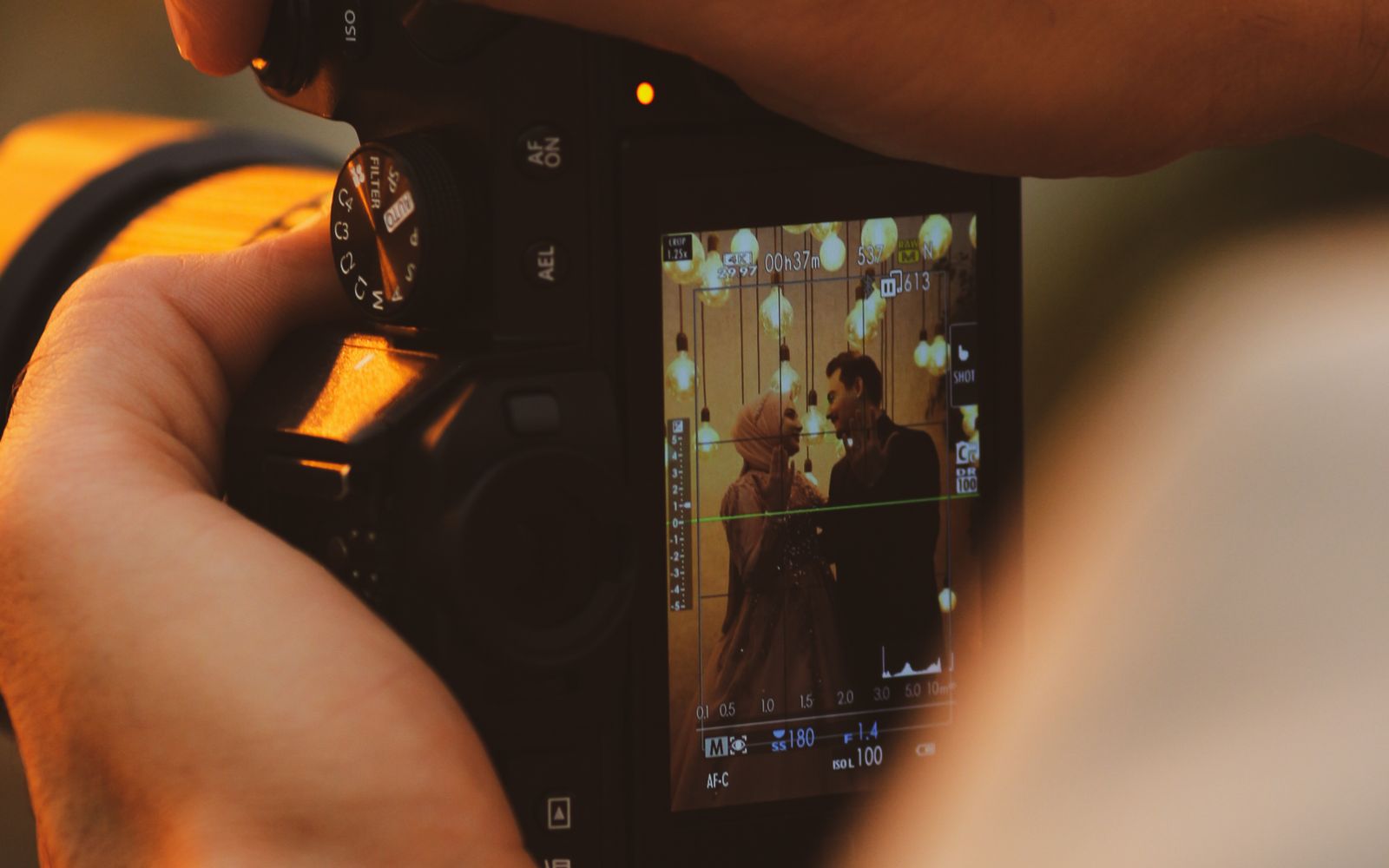 A wedding photographer holding a camera with a couple framed on the screen in warm light